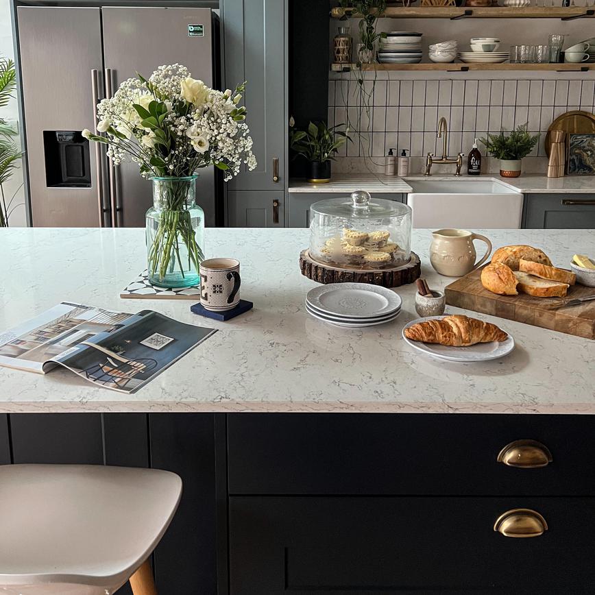 White quartz worktop on a navy shaker kitchen island, showing antique brass cup handles, flowers, and dusk blue wall units.