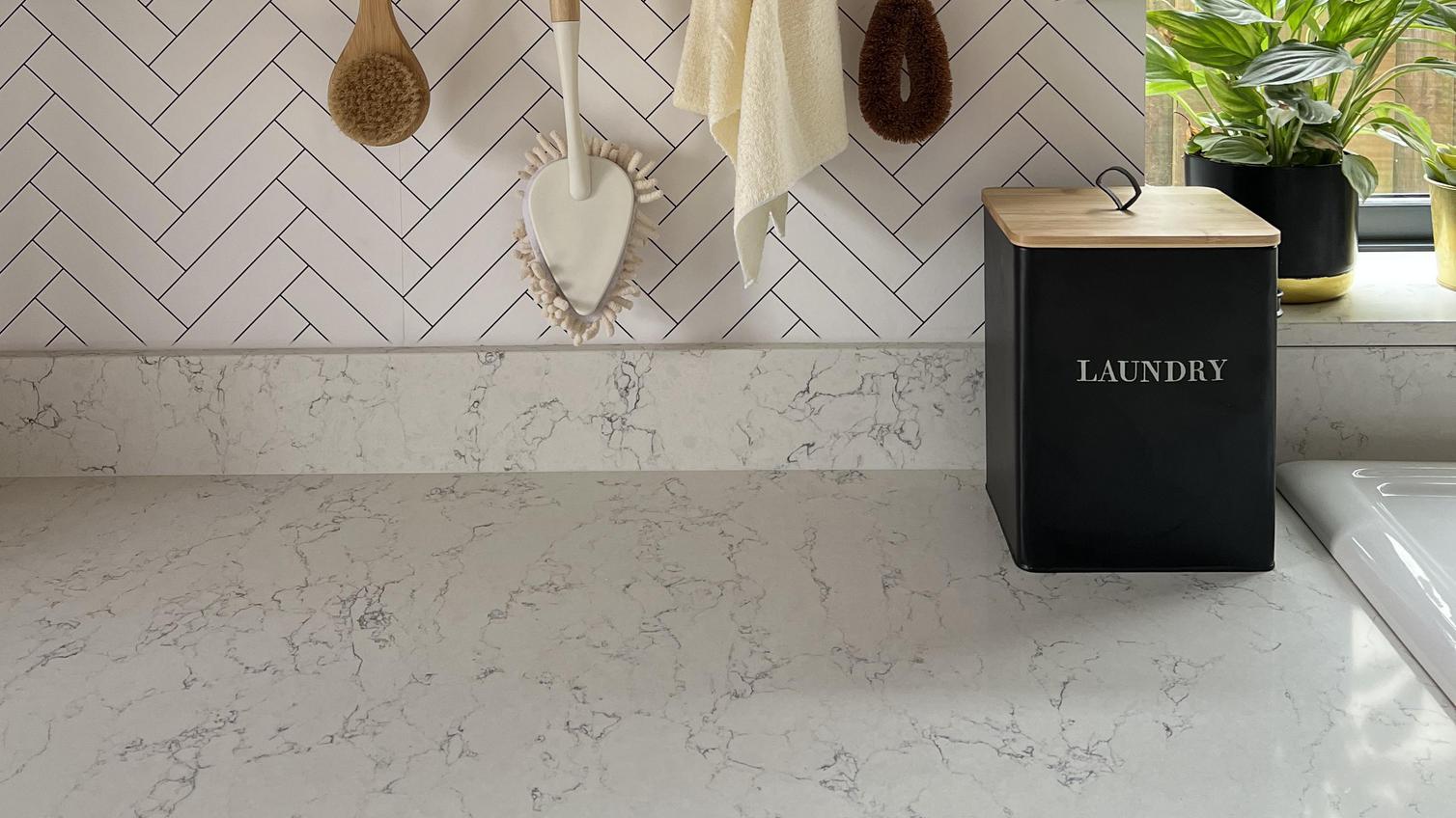 A slim, white, quartz worktop and upstand with a marble-effect pattern and glossy finish for a luxurious utility room idea.