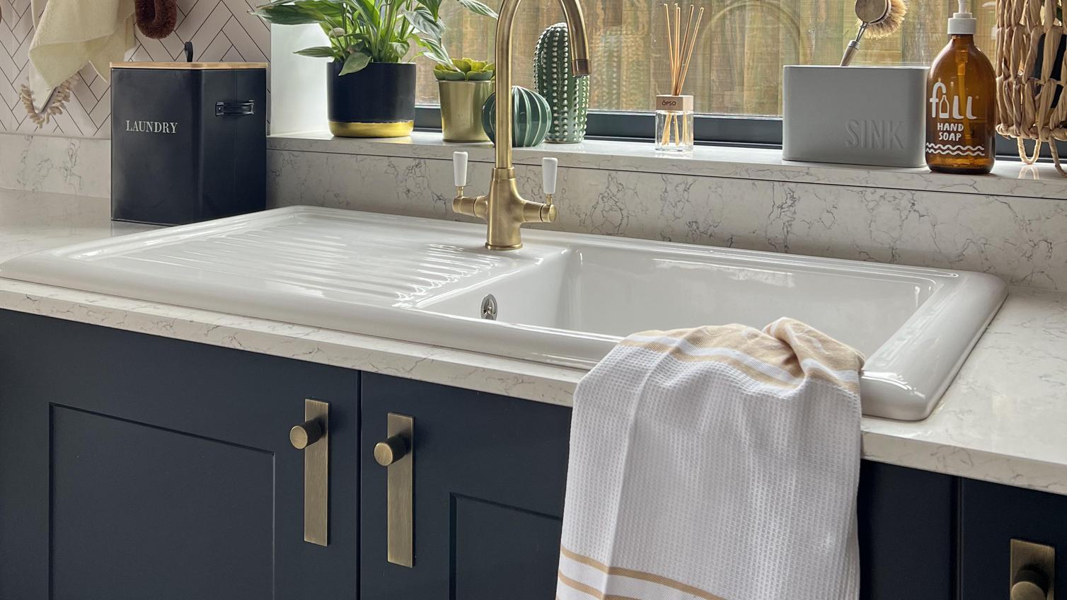 Simple utility room idea using a white, single-bowl sink and a brass, swan-neck tap. Includes white worktops and navy units.