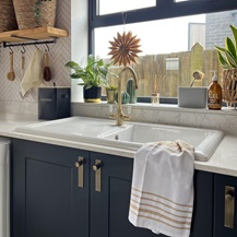 Simple utility room idea using a white, single-bowl sink and a brass, swan-neck tap. Includes white worktops and navy units.