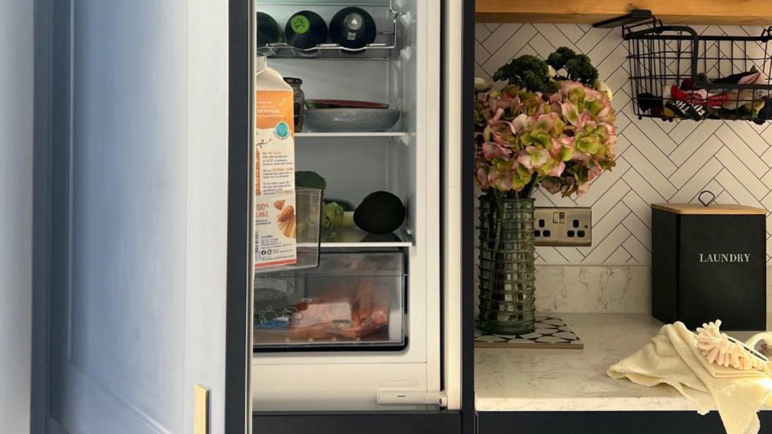 A sleek utility room idea using a 70/30, integrated fridge freezer. Includes navy shaker kitchen doors and brass handles.