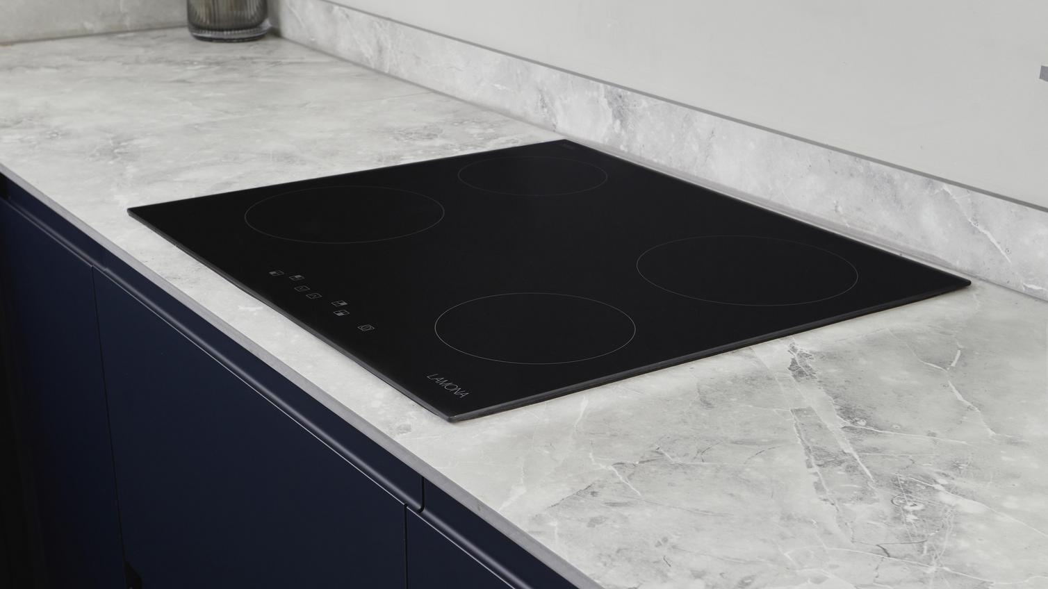A black, electric Lamona hob, inset into a white marble-effect worktop. Behind the hob is a matching white upstand.
