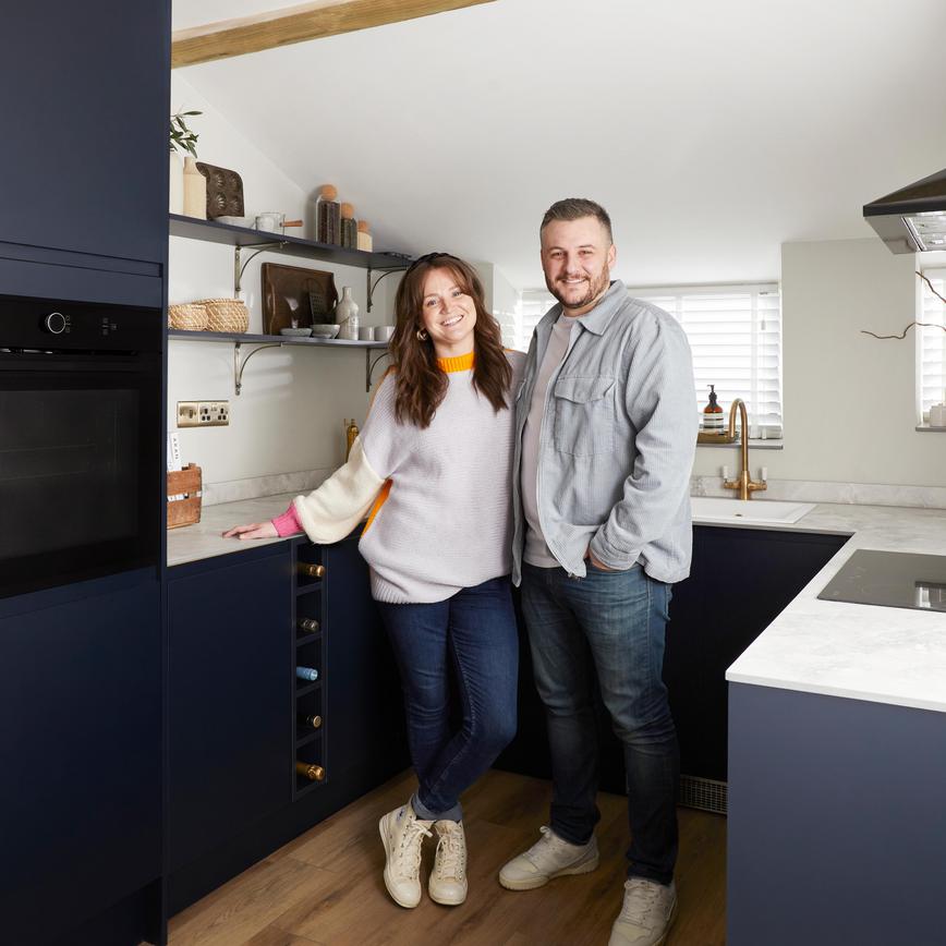 Influencers Grace and James standing in their Clerkenwell matt navy kitchen, with an integrated oven, hob, and extractor.