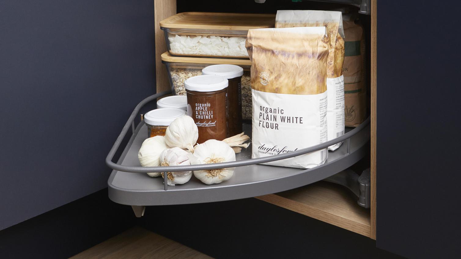 Integrated pull-out storage accessory is fitted into a corner kitchen cabinet. The storage features dried goods & food tins.