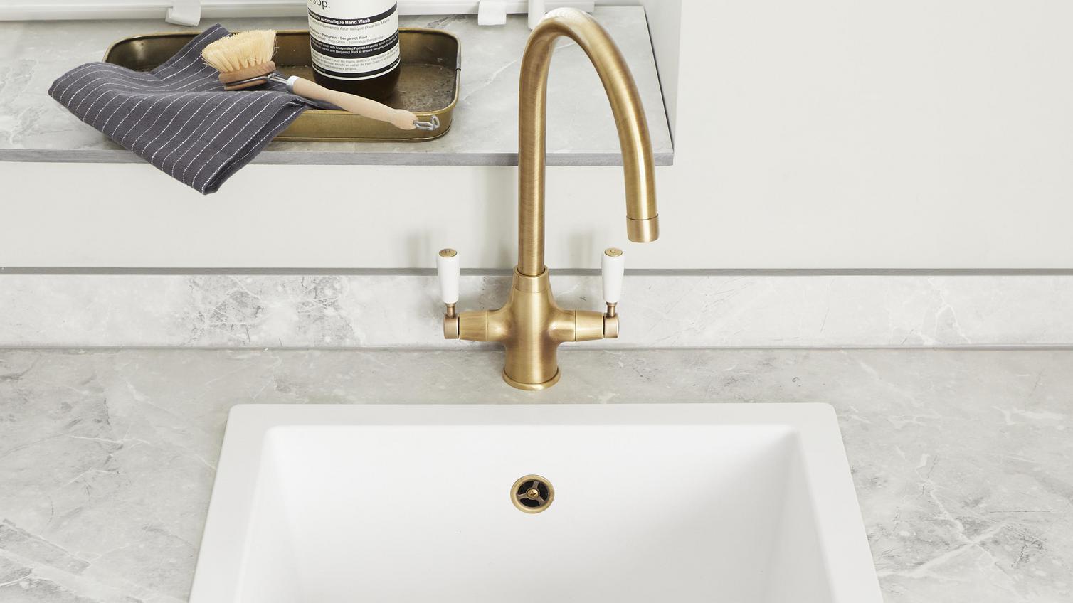 A classic-style brass tap and matching strainer in a white inset sink. The tap features two-lever control and a curved spout.