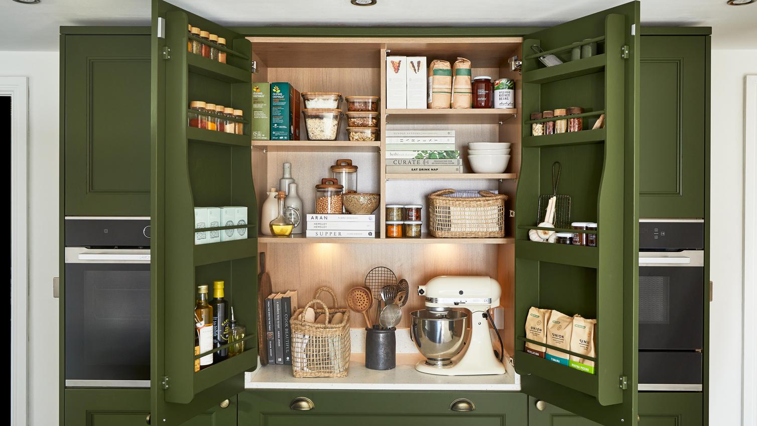 An olive green kitchen larder cabinet, which has matching door balconies for storage. Inside are oak-effect shelves.
