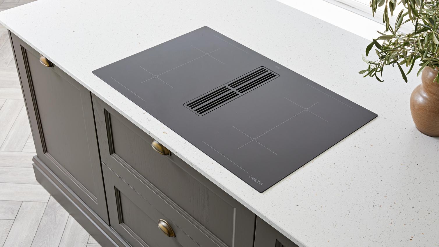 A black, integrated induction hob with a built-in extractor. It is fitted in a brown kitchen island in a white worktop.