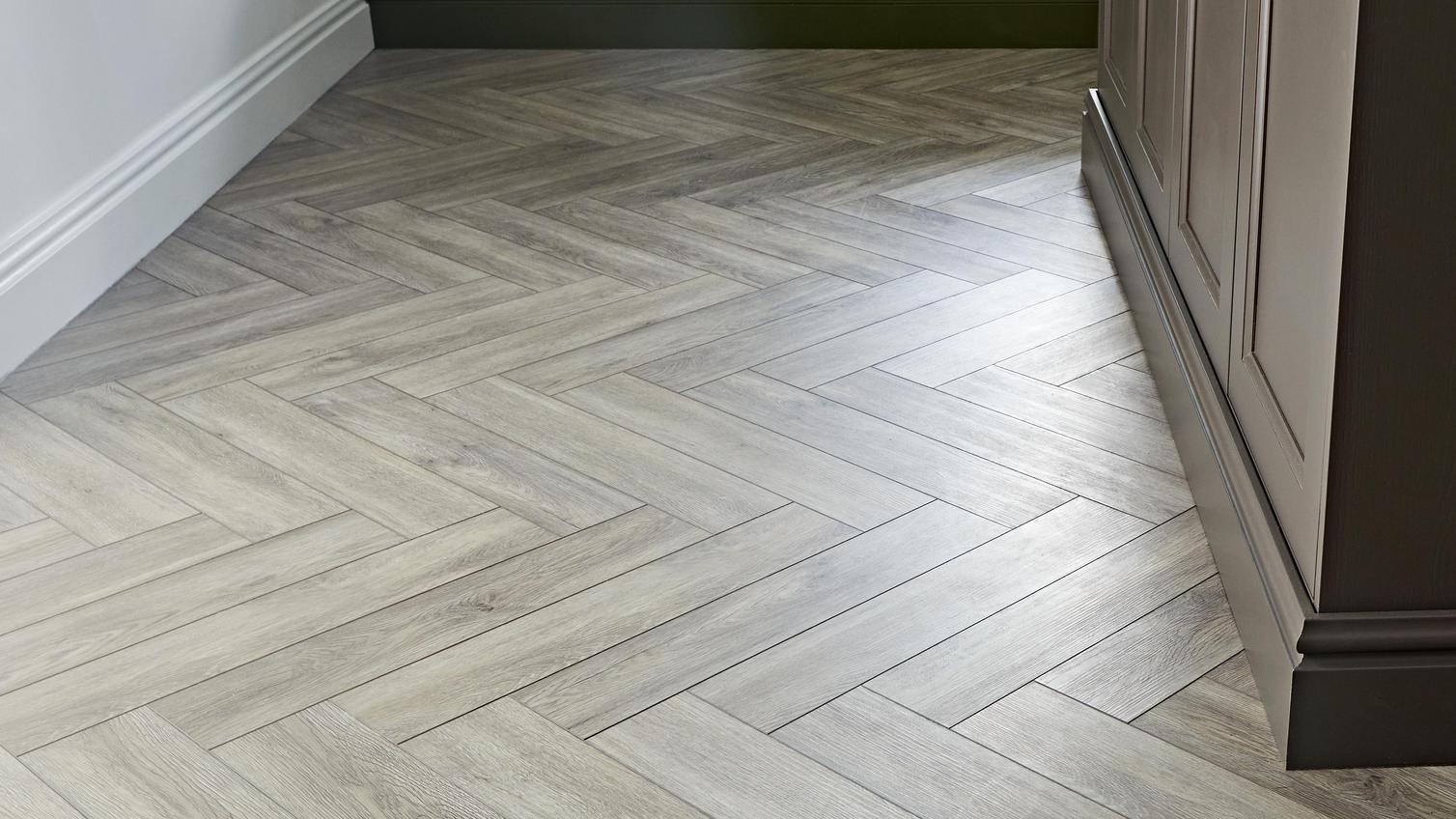 Oak-effect vinyl flooring in a chevron-style layout. It is fitted alongside brown and green kitchen cabinets.