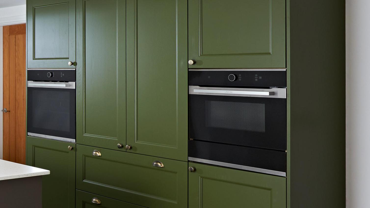 Black Lamona appliances integrated into tall cabinets. The units have olive green door fronts in a shaker style.