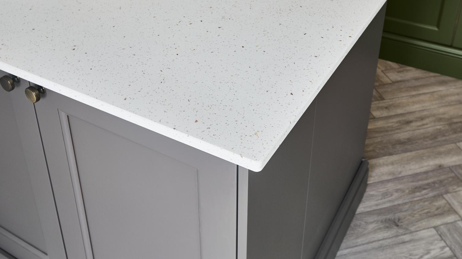 A white bespoke acrylic worktop on a brown-tone kitchen island. The door fronts have a shaker design and brass handles.