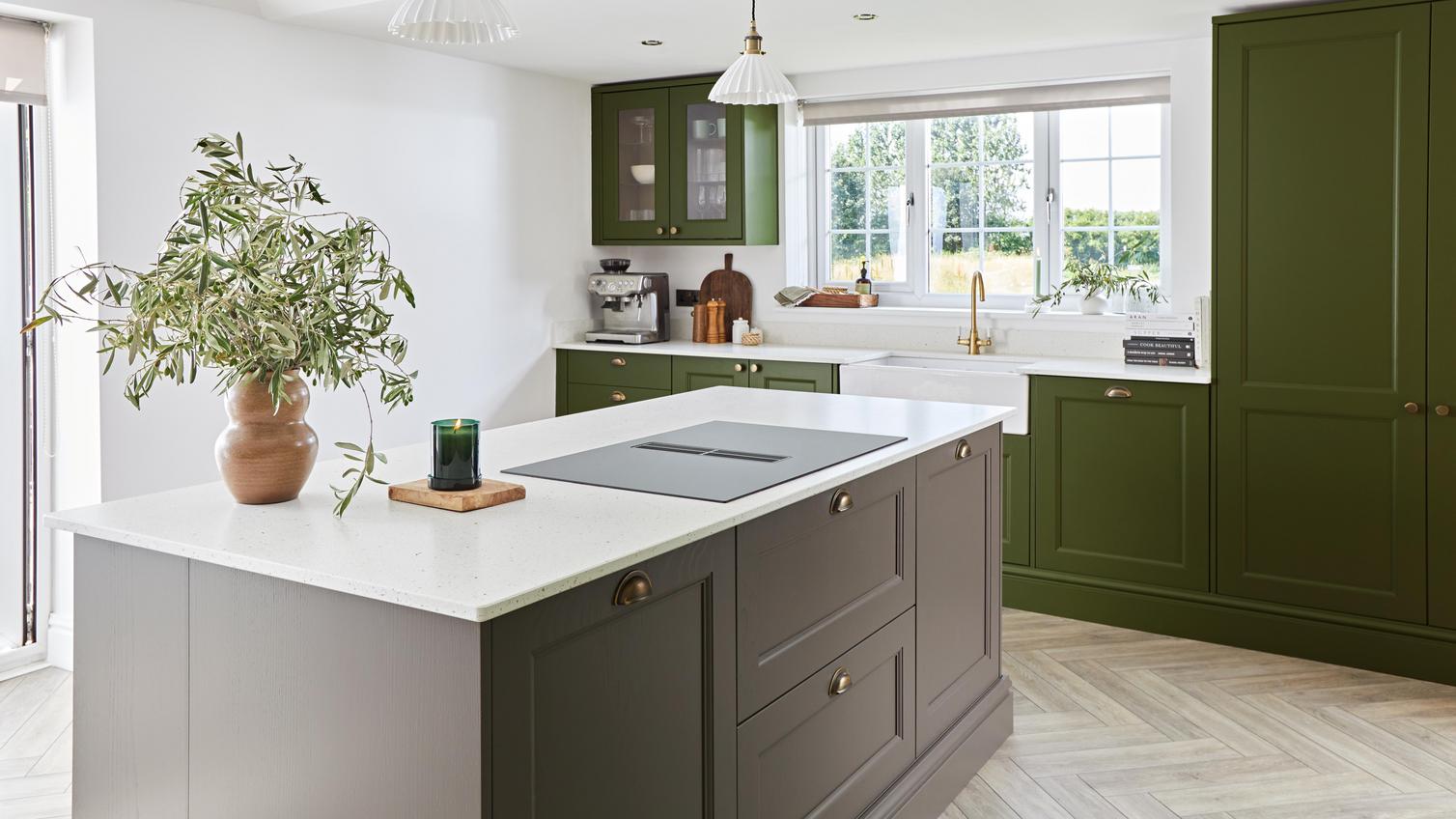 An olive green shaker kitchen with a truffle brown kitchen island. There are white bespoke worktops and brass handles.
