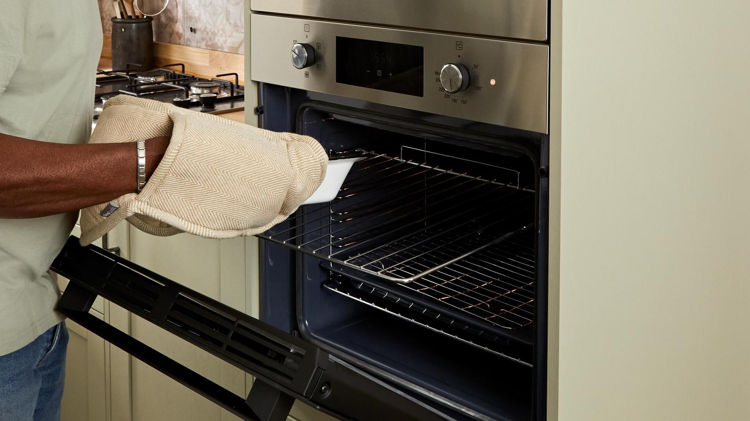 Victor in the kitchen putting a dish into a black, built-in oven, which is fitted at eye level into an appliance tower unit.