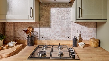 Sage-green kitchen with shaker doors and pelmets for a decorative look. Features a four-burner gas hob and black handles.
