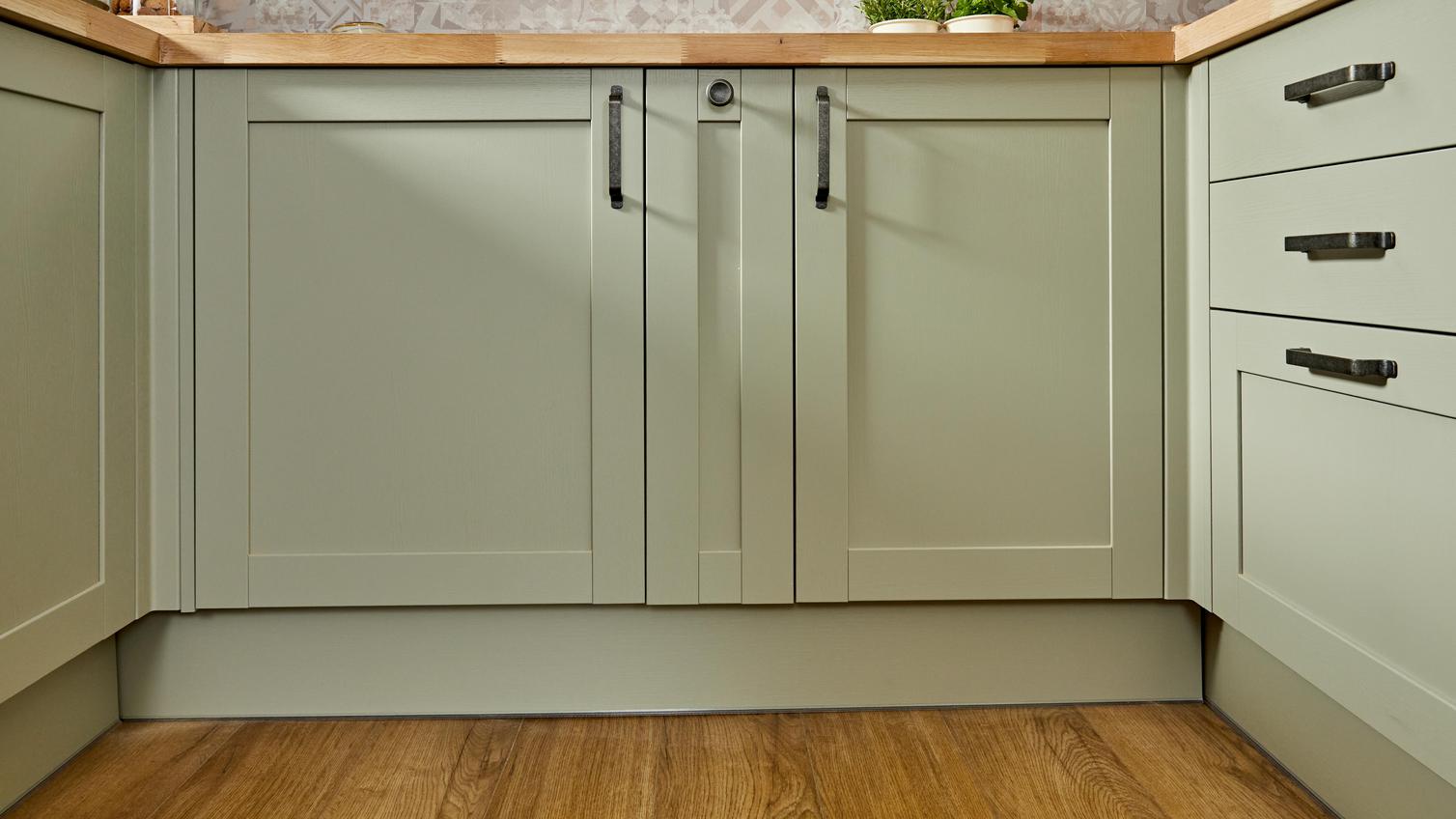 A sage-green shaker kitchen in a u-shaped layout featuring black, D-shaped handles, timber worktops and wood-effect floors.