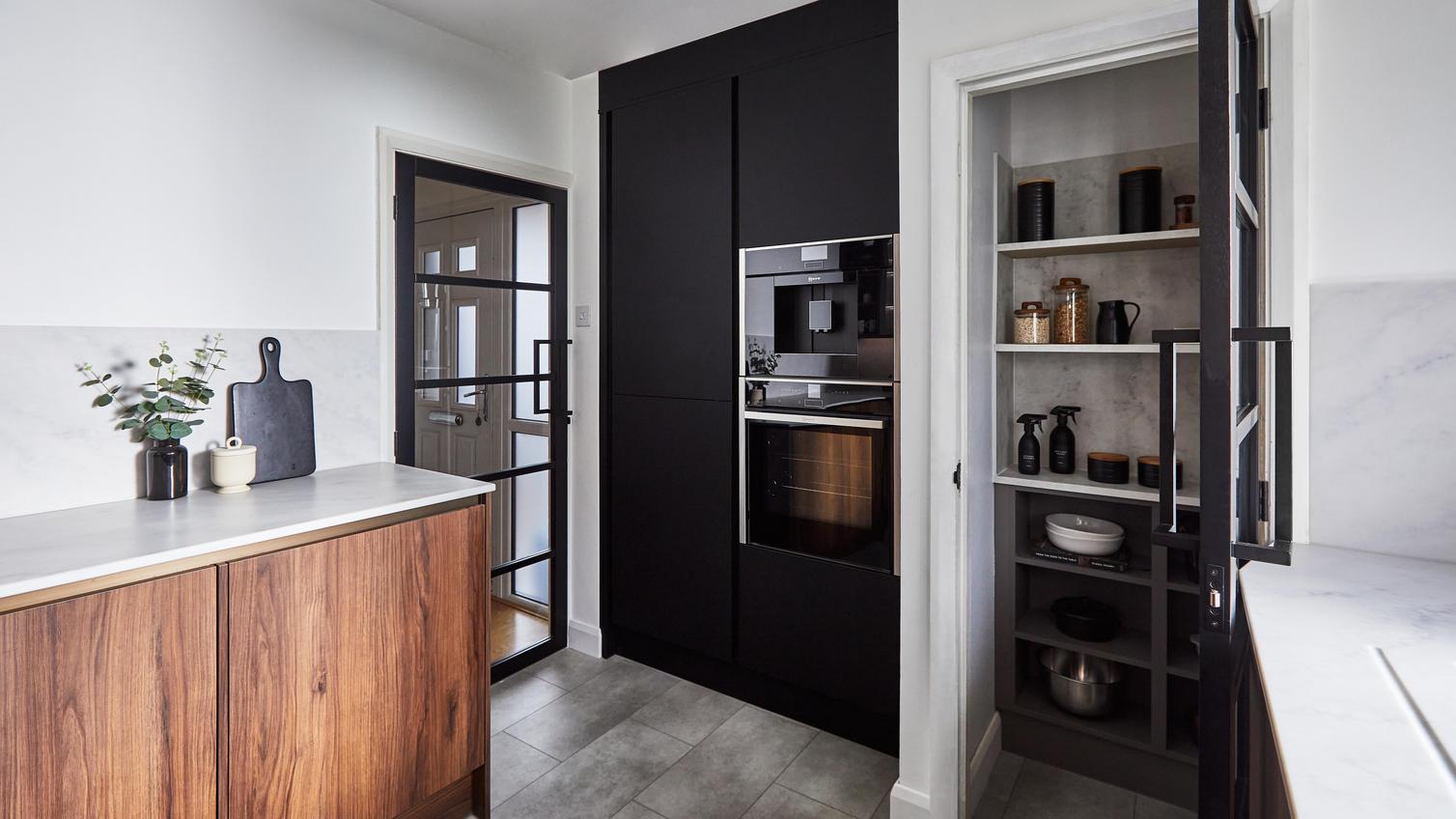 Contemporary kitchen featuring walnut and black cupboards in a slab design. Has a pantry with open shelves and a glass door.