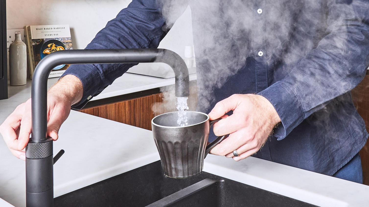 Man in a blue shirt using a boiling water, black tap with an angled spout.