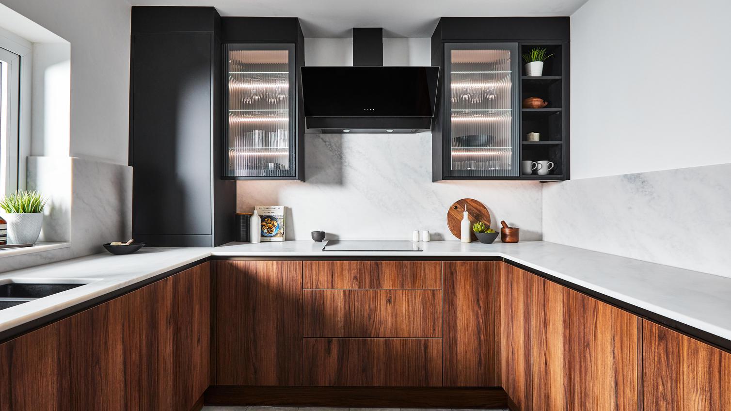 A modern luxury kitchen featuring walnut and black cupboards doors in a slab style. The kitchen also contains white worktops.