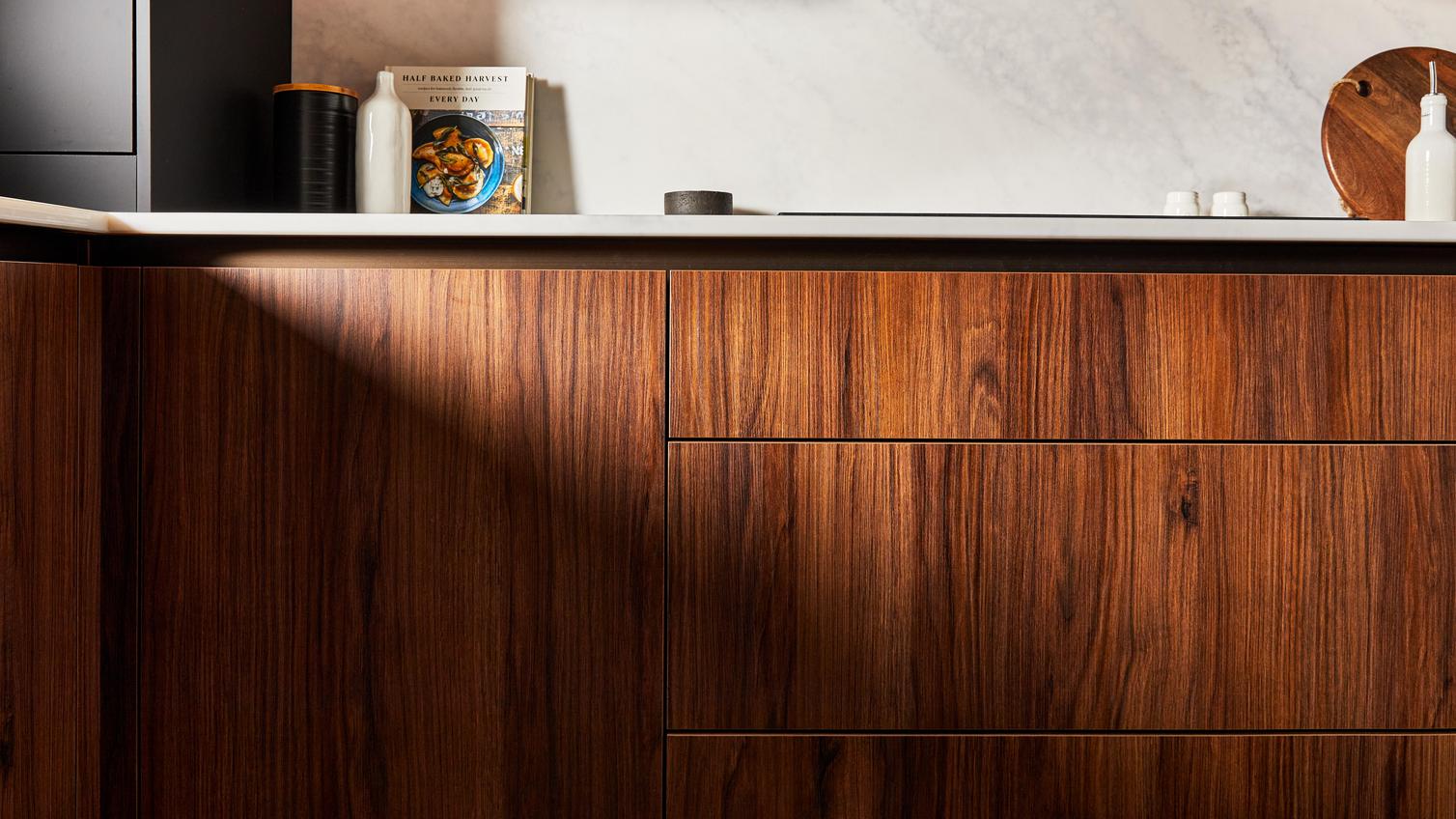 A modern luxury kitchen featuring walnut cupboard doors in a slab design, handleless units, and bespoke white worktops.