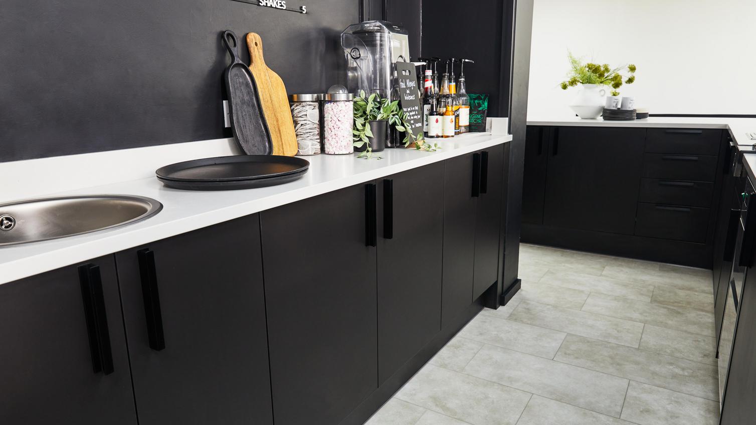 Jill Scott Cafe Kitchen Makeover featuring a black, slab kitchen with a smooth finish. Includes white worktops and tile floors