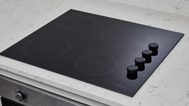 Jill Scott Cafe Kitchen Makeover with a black, Lamona induction hob with four knobs on the right side. Fitted to a white worktop.