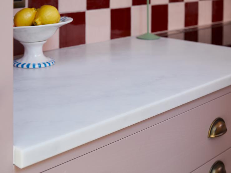 A bespoke, white quartz worktop fitted to the top pink shaker kitchen cabinets. They are styled with metallic handles.