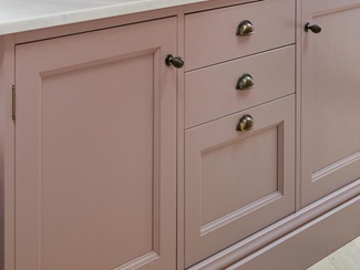 A pink kitchen island with in-frame doors and drawers. It is finished with a bespoke quartz worktop and metallic handles.