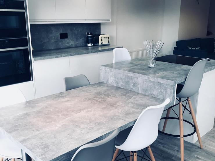 Grey concrete effect kitchen island with white gloss cupboards and six white and grey chairs
