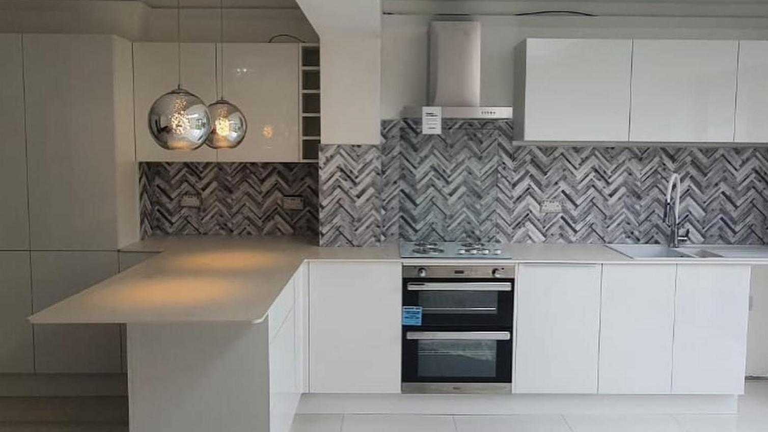 A large white kitchen idea with slab cupboards. Includes a silver chimney cooker hood, and a herringbone-effect backboard.