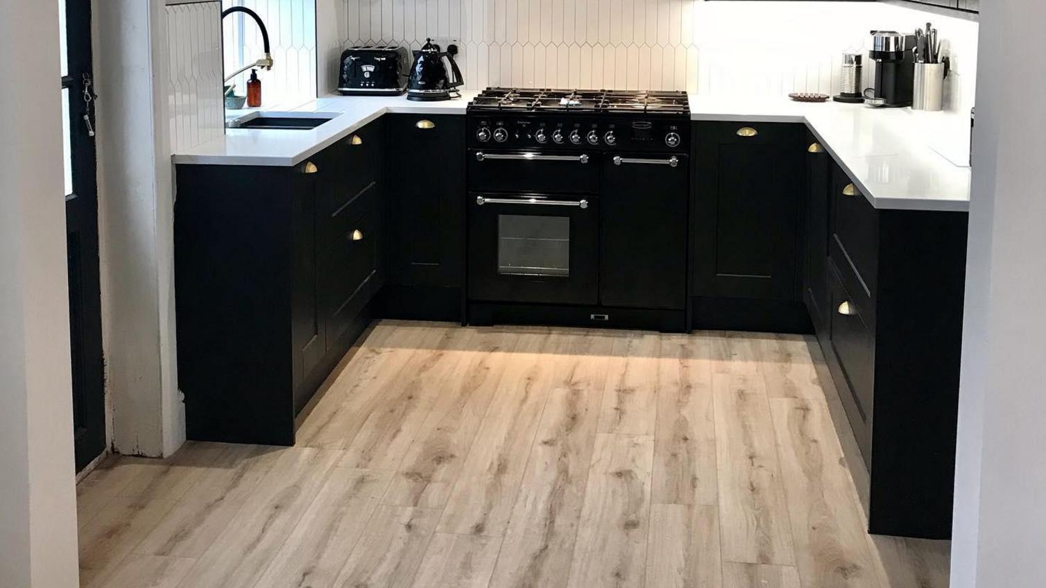 Black painted kitchen idea with shaker cupboards, pale oak floors, and white worktops.