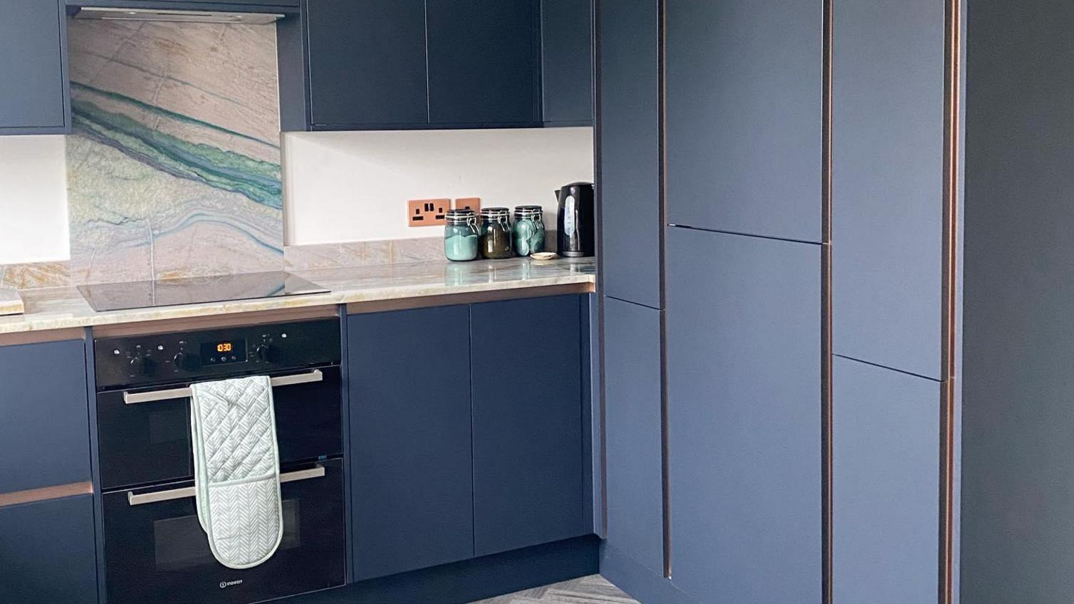Navy integrated handle kitchen with a marble backsplash with blue veining, an integrated oven and tower units.