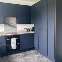 Navy integrated handle kitchen with a marble backsplash with blue veining, an integrated oven and tower units.