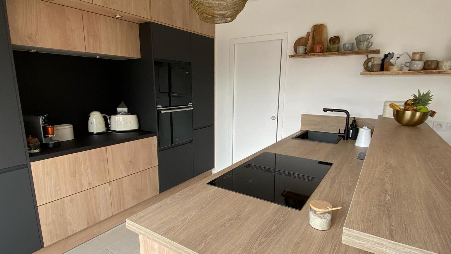 Black and oak kitchen design with slab doors, a light oak kitchen island with an induction hob, black sink and tap, and oven.