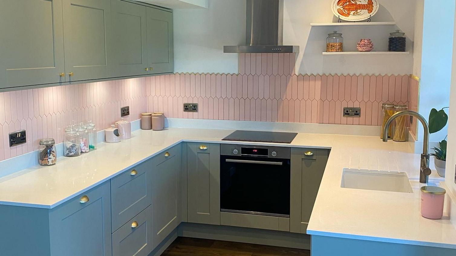 Light grey kitchen idea with shaker cupboards, brass cup and knob handles, a pink tiled backsplash and silver appliances.