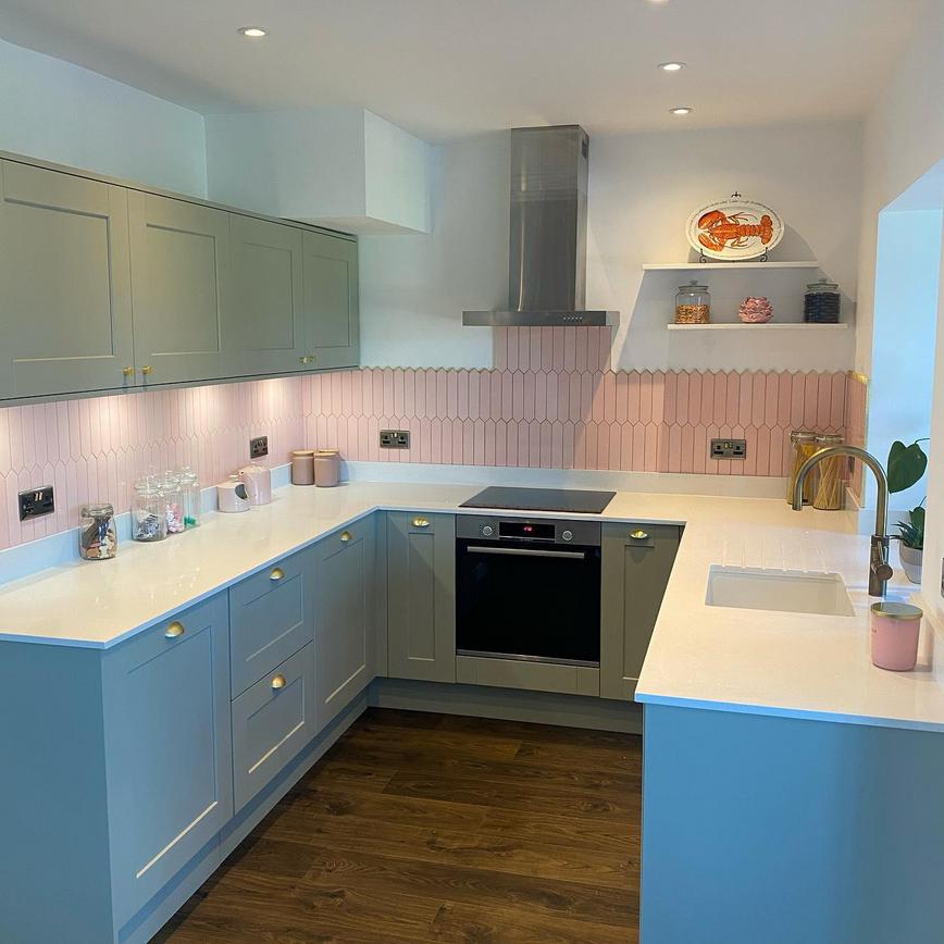 Light grey kitchen idea with shaker cupboards, brass cup and knob handles, a pink tiled backsplash and silver appliances.