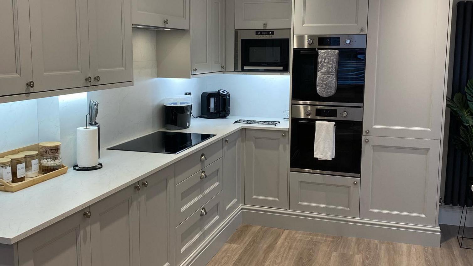 A luxurious grey kitchen idea featuring grey shaker units with a beaded detail. Includes timer floors and white worktops.