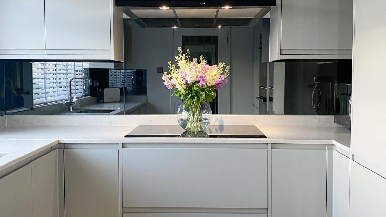 A modern budget kitchen idea using gloss grey integrated handle kitchen doors, white worktops, and LED plinth lighting.
