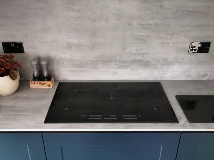 Black induction hob set on a grey concrete effect worktop with a matching backboard and navy shaker handleless cupboards.