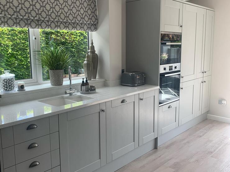 Grey single wall kitchen idea with shaker cupboards, silver cup handles, a white worktop and inset sink, and grey oak floors.