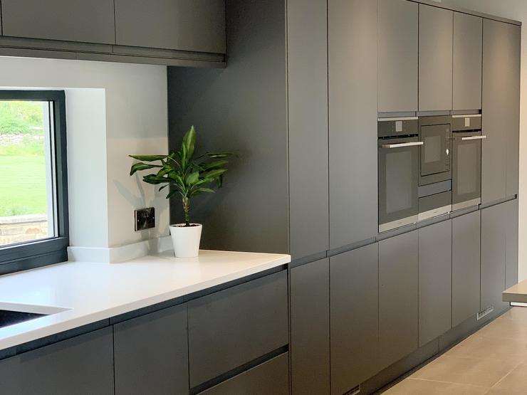Black single wall kitchen idea with integrated handle cupboards, a white worktop and integrated appliances in a tower format.