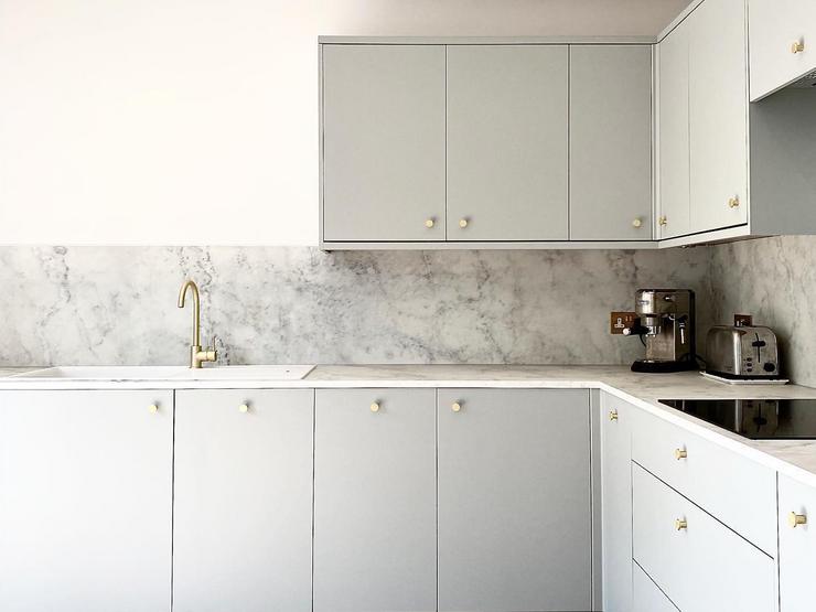 Grey L-shaped kitchen idea using slab cupboard doors, marble-effect backboards, and brass knob handles for a luxe look.