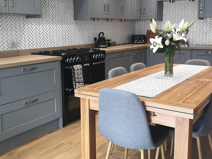 An L-shaped kitchen diner with dark-grey shaker cupboard doors. Includes a black range cooker and an oak dining table.
