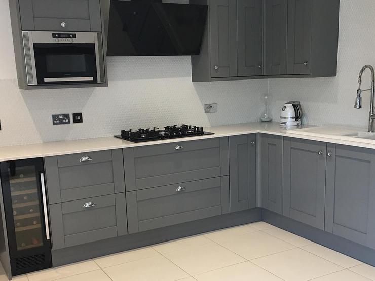 A large L-shaped kitchen idea that has shaker cupboards and white worktops. It also has a black wine cooler and a gas hob.