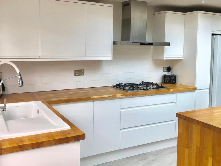 White integrated handle kitchen, with a gloss finish, warm oak worktops and grey flooring.