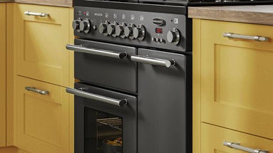 Yellow paintable kitchen with shaker cupboards, featuring a light oak floor, silver bar handles and a black rangemaster oven.
