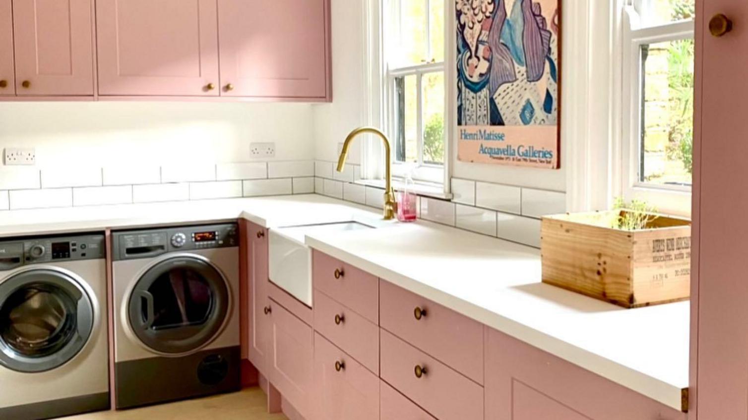 Pink shaker kitchen design in an l-shape, with brass knob handles, white worktops, washer appliances, and a gold tap.