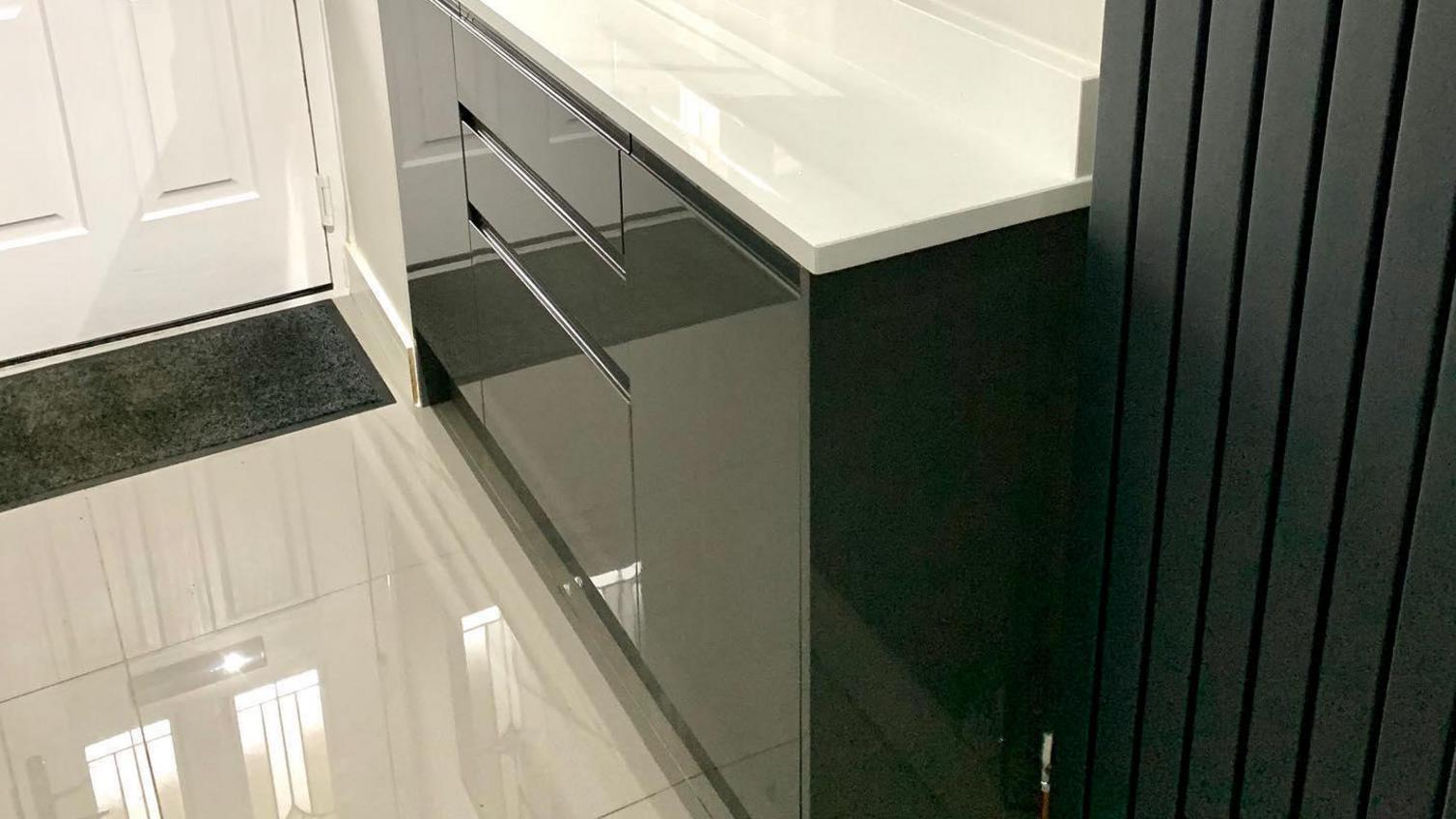 Black boot room ideas using glossy kitchen doors with integrated handles in graphite. Includes white worktops and floors.