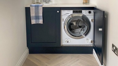 Small boot room idea with navy shaker cabinets, chevron flooring, and a white integrated washing machine.