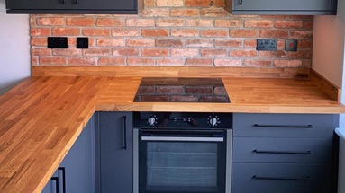 Matt black modern kitchen with slab cupboard doors. Includes a black induction hob and handles, and an oak worktop.