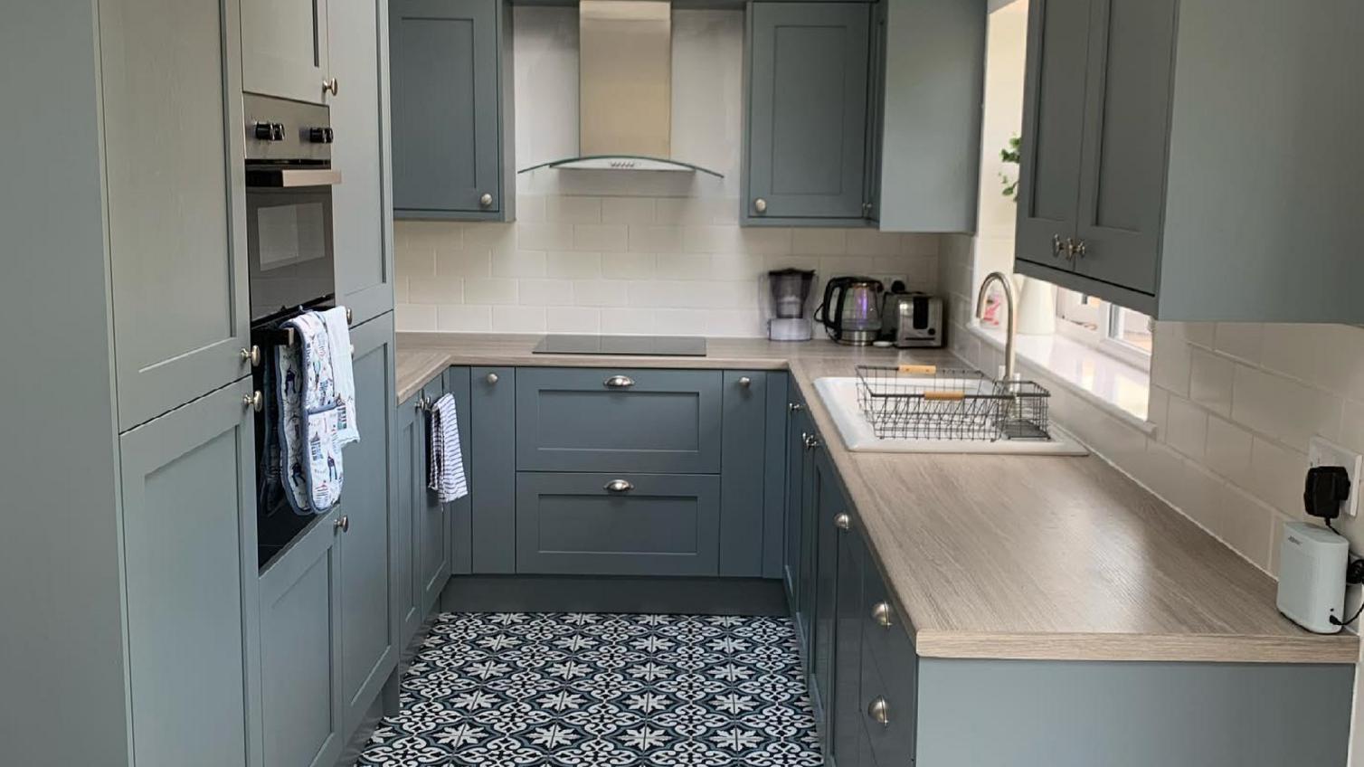 A blue shaker kitchen idea with dusk-blue Chilcomb shaker cupboard doors and brown wood-effect worktops in a u-shaped layout.