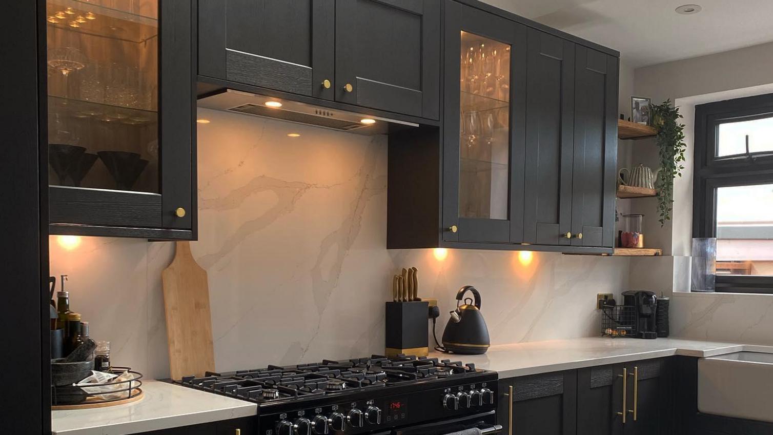Black shaker style kitchen with glass dresser units, a black range cooker, white marble worktops.